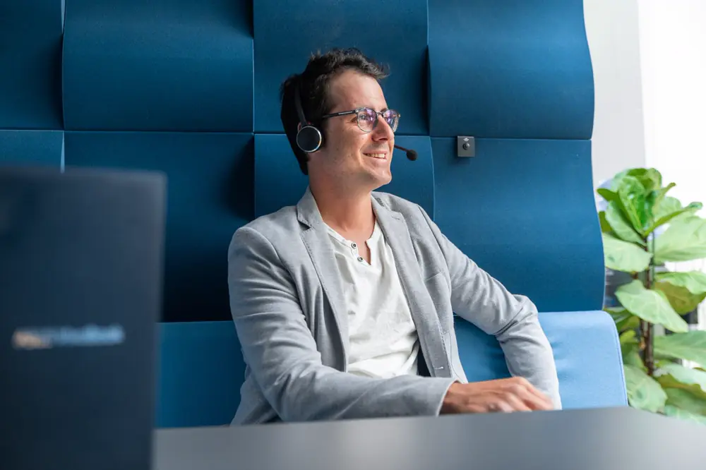 Stephan Gasser von Telemarketing Schweiz telefoniert mit Headset in einer blauen Akustikkabine für persönliches B2B Telemarketing