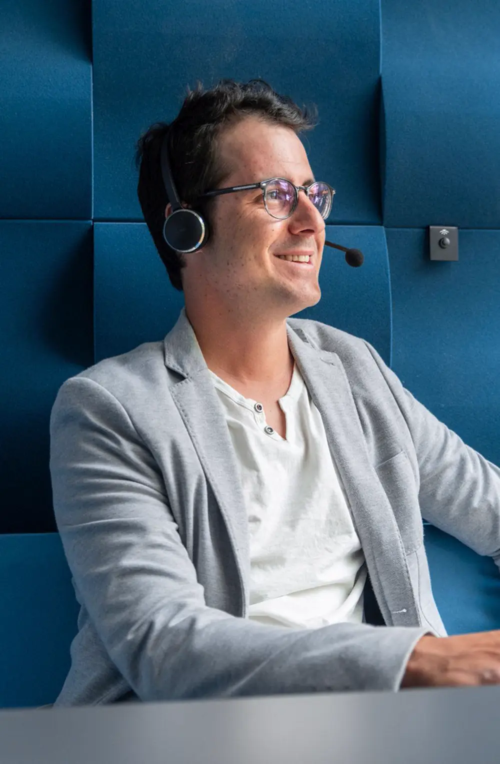 Stephan Gasser telefoniert bei der B2B-Telefonakquise mit Headset in einer blauen Akustikkabine und lächelt