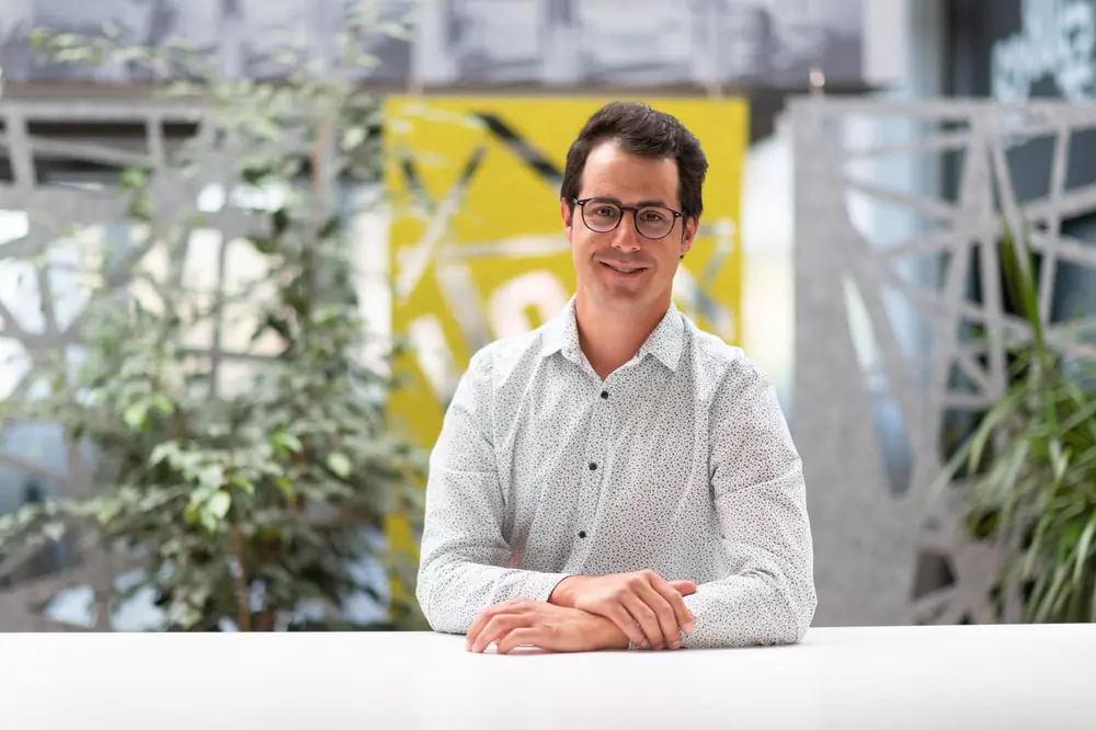 Stephan Gasser, Ansprechpartner für B2B Telemarketing in der Schweiz, sitzt mit verschränkten Händen an einem weissen Tisch und lächelt